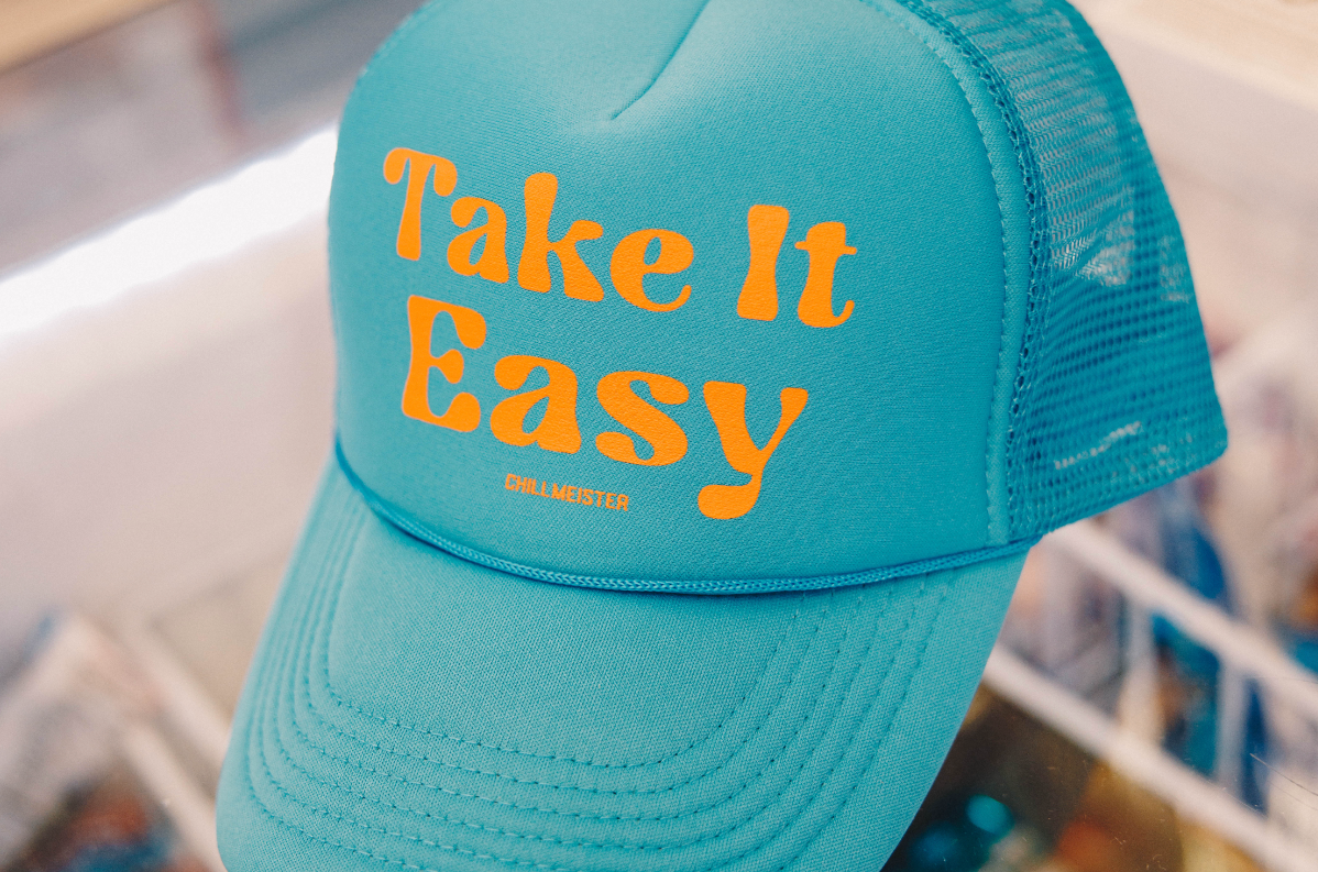 A bright turquoise cap with the phrase "Take It Easy" in bold orange letters, resting on a display.